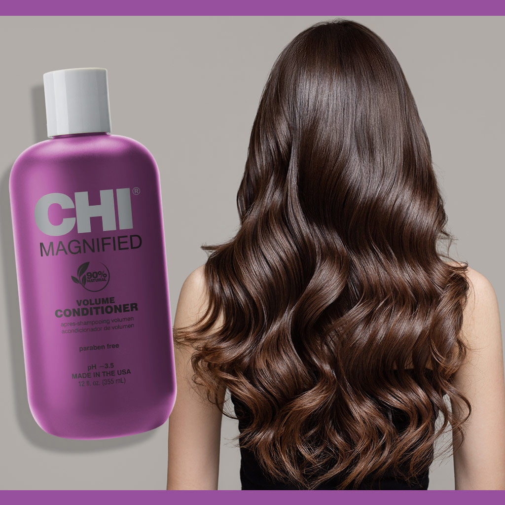 Purple CHI Magnified Volume Conditioner bottle next to a person with long, wavy hair on a gray background