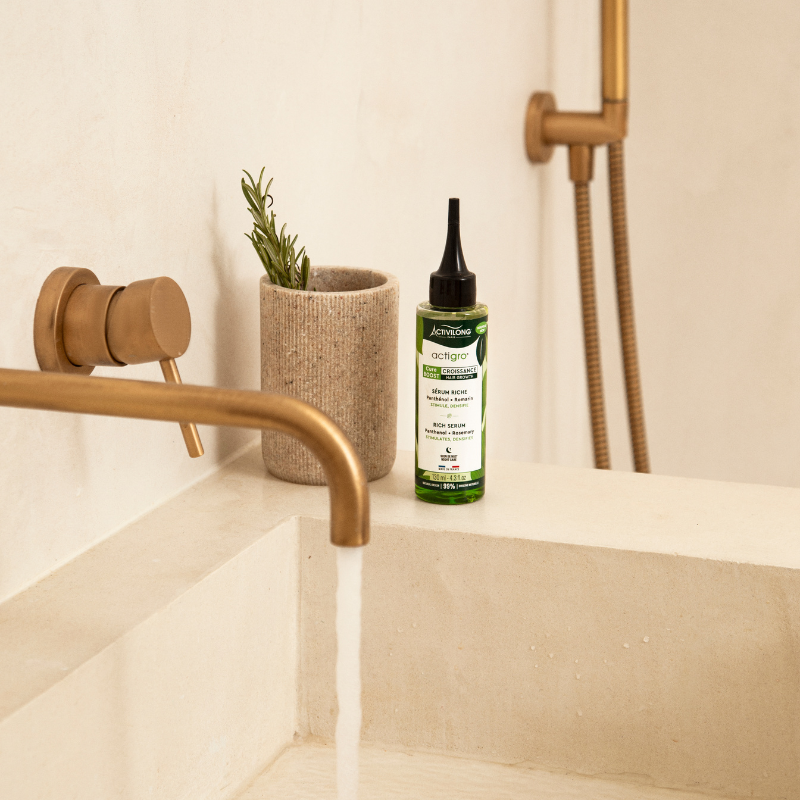 ACTIVILONG ACTIGRO Sérum Riche 130 ml bottle by ABS France Wholesale on a bathroom counter with gold faucet and plant