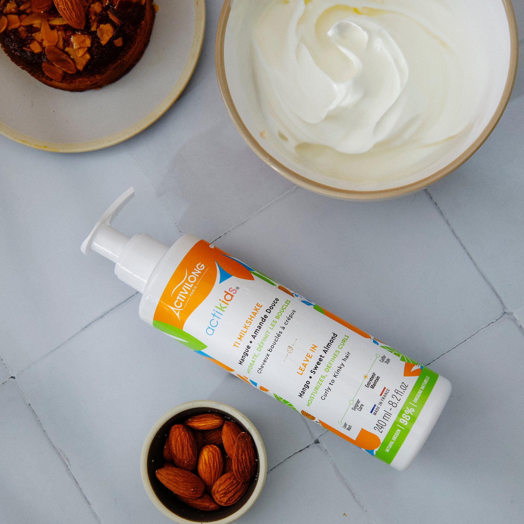 ACTIVILONG ACTIKIDS Ti Milkshake Leave-In 250ml bottle by ABS France Wholesale on a tiled surface with almonds and a dessert.