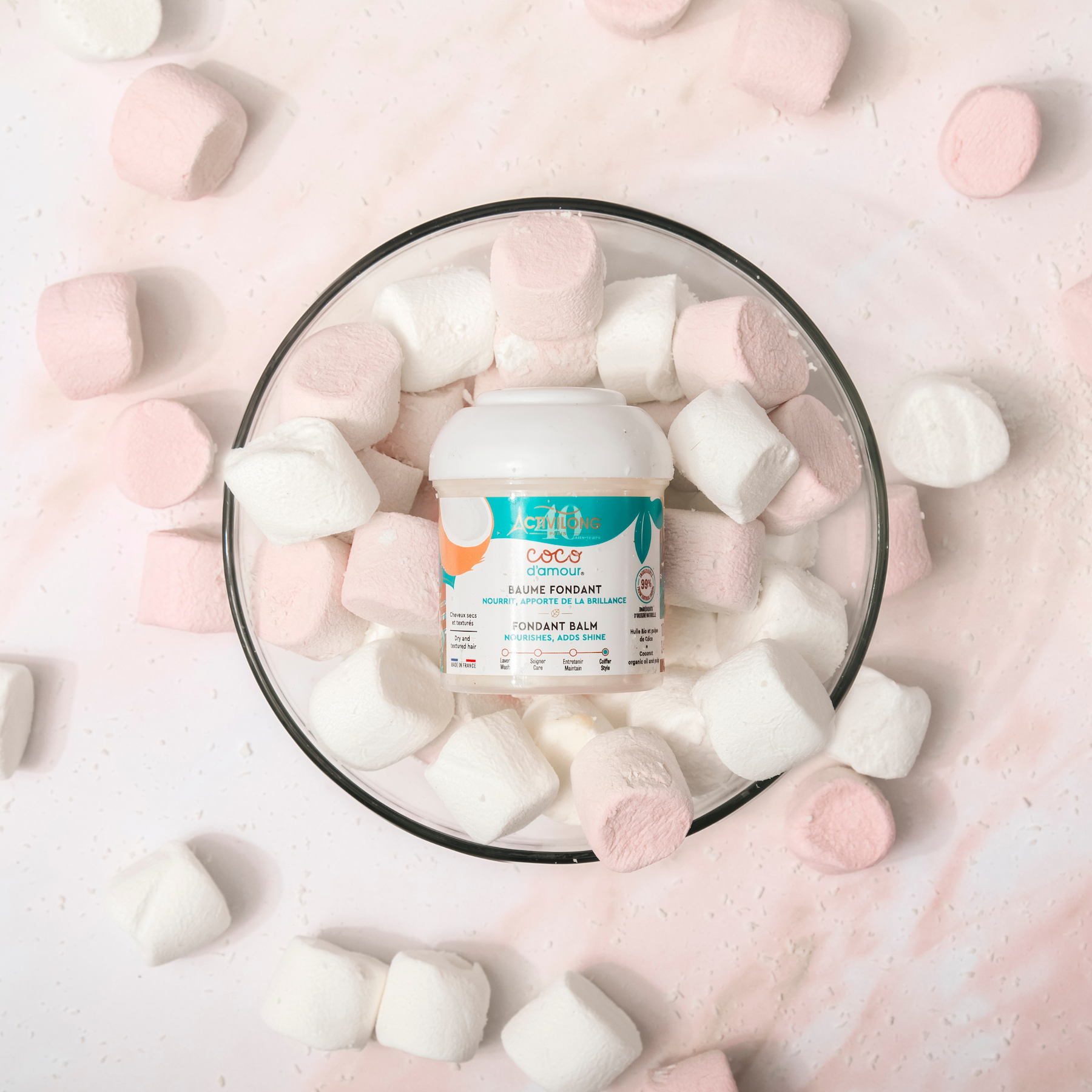 Jar of ACTIVILONG COCO D’AMOUR Baume Coiffant Fondant 100ml by ABS France Wholesale surrounded by marshmallows on a soft pink background