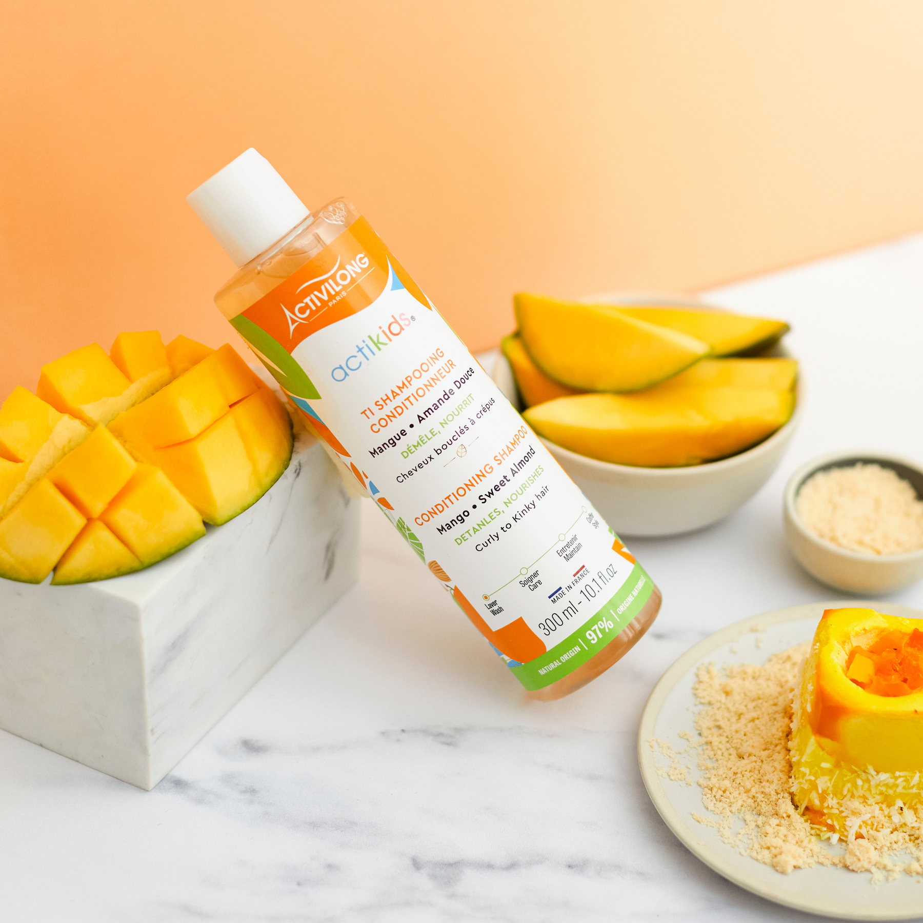ACTIVILONG ACTIKIDS Ti-Shampooing Conditionneur 250ml bottle by ABS France Wholesale with mango slices and a smoothie on a marble surface.