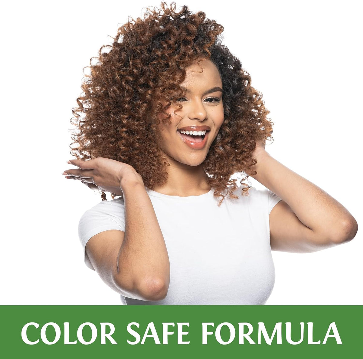 A smiling woman with voluminous brown curly hair wearing a white t-shirt, posing with her hands near her hair against a white background, with a green banner at the bottom reading 'COLOR SAFE FORMULA'.