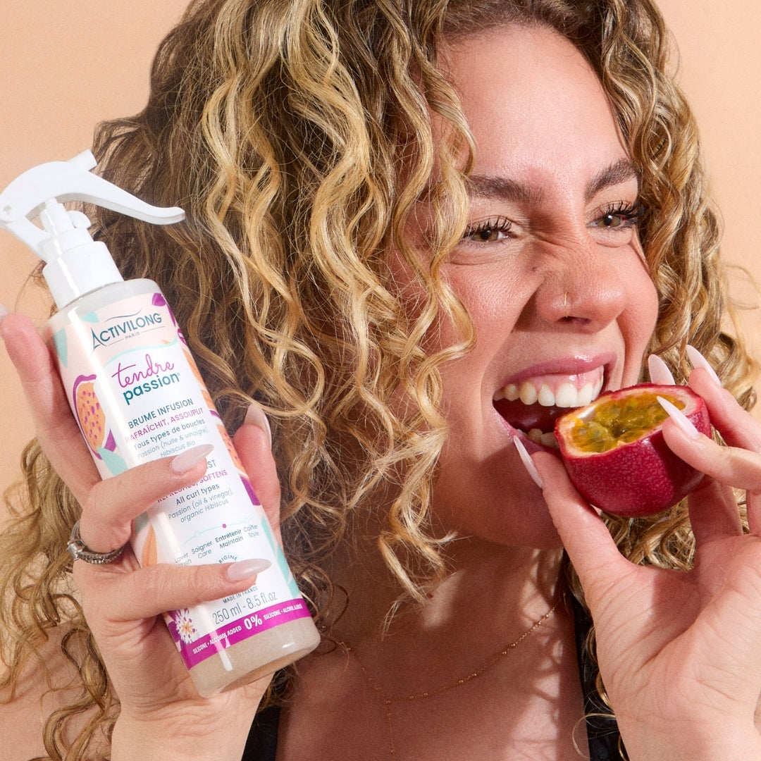 Woman eating a passion fruit while holding an ACTIVILONG TENDRE PASSION Brume Infusion 250ml spray bottle by ABS France Wholesale.