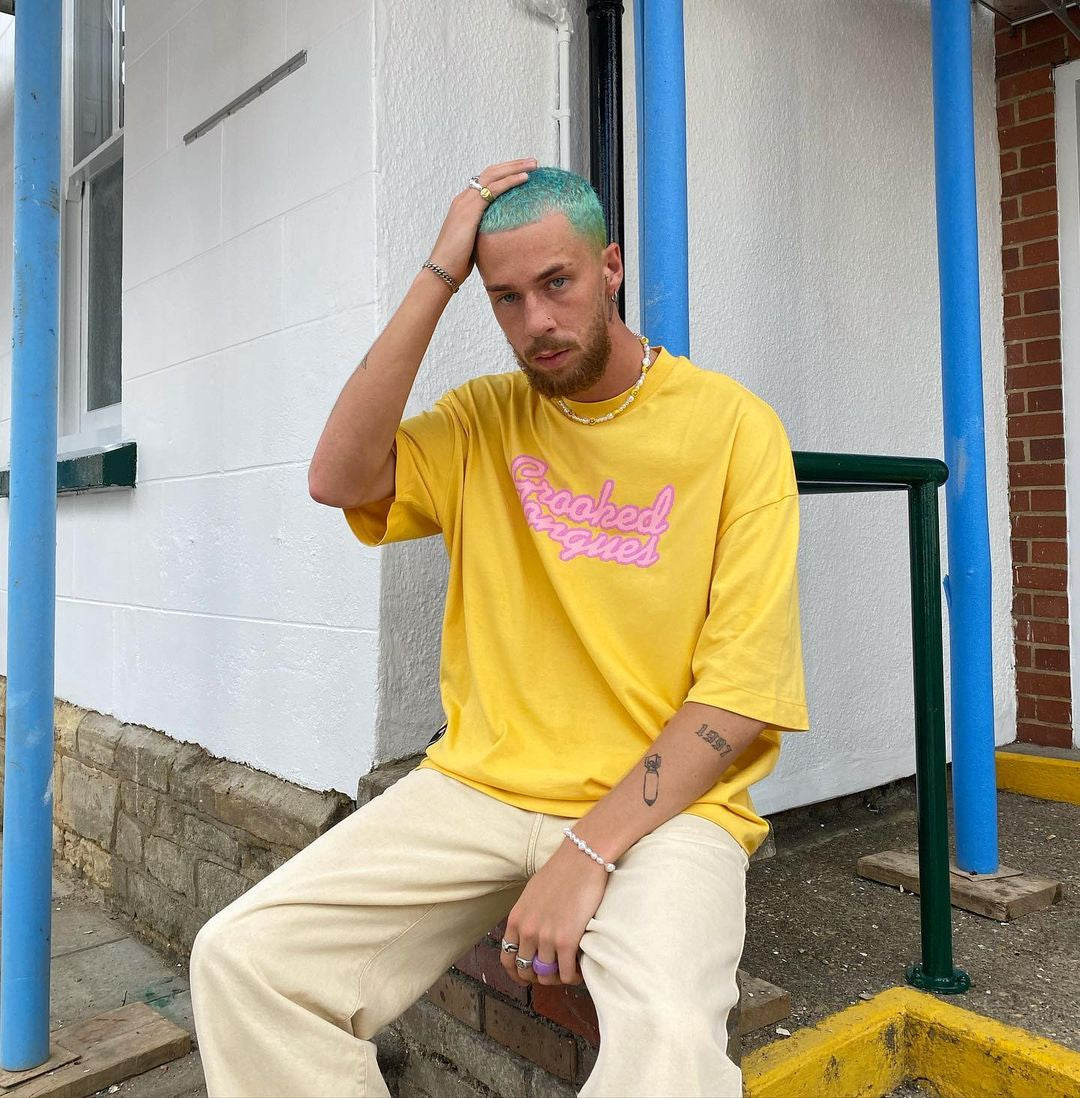 Crazy Color's Person wearing a yellow t-shirt with pink text, sitting on steps outdoors by ABS France Wholesale