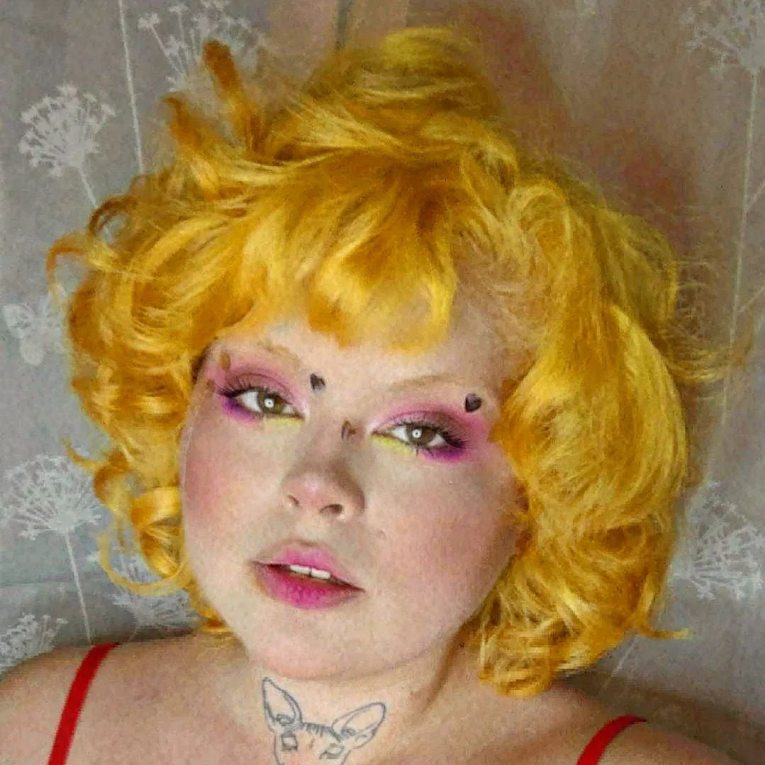 Crazy Color's Person with bright yellow hair and colorful makeup against a textured wall by ABS France Wholesale