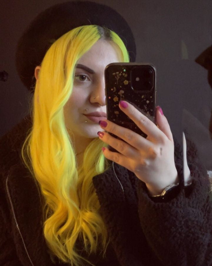 Crazy Color's Person with yellow hair holding a phone in a dark setting by ABS France Wholesale