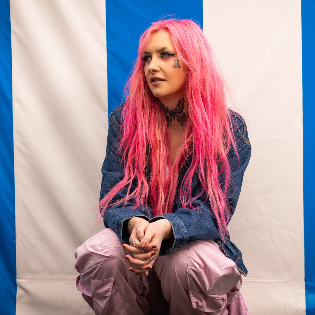 Crazy Color's Person with pink hair and denim jacket sitting against a striped background by ABS France Wholesale