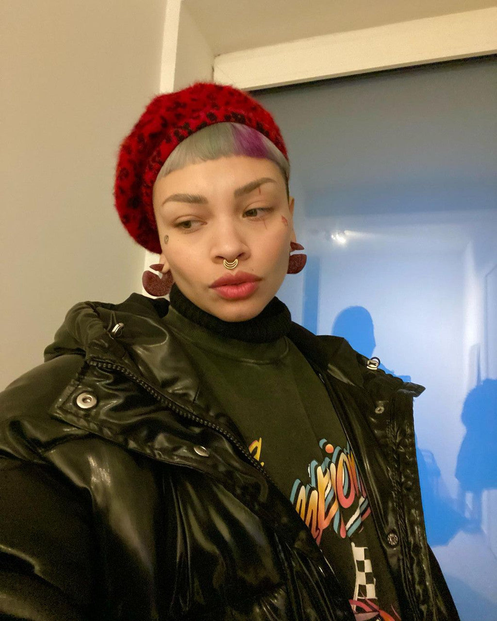 Crazy Color's Person wearing a red beanie and black jacket with colorful text, standing indoors by ABS France Wholesale