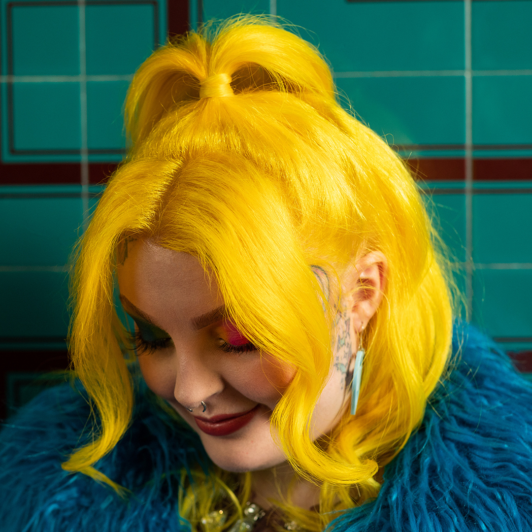 Crazy Color's Person with bright yellow hair styled in a high bun, wearing a blue fur coat against a tiled wall by ABS France Wholesale