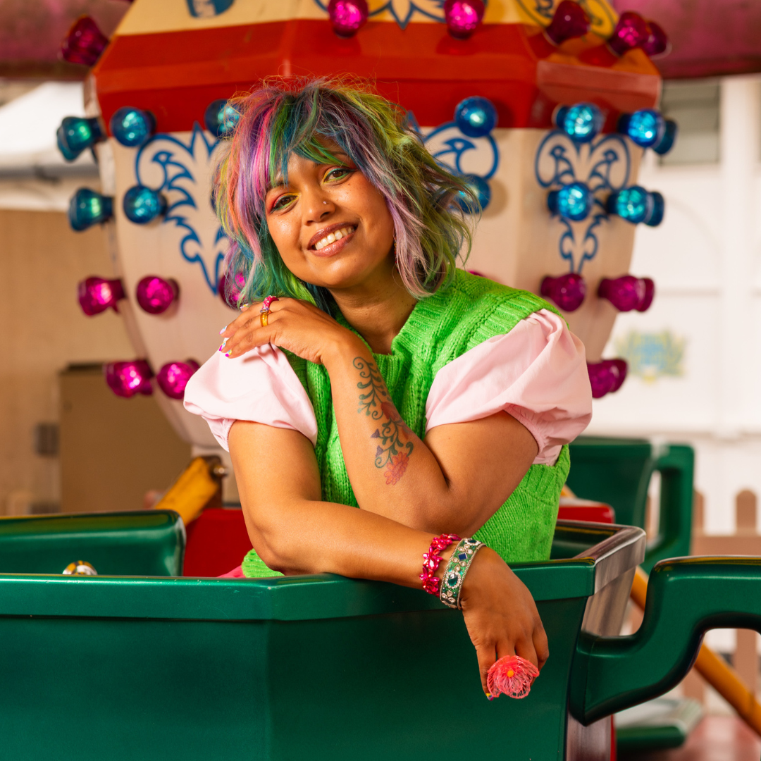 Crazy Color's Person with colorful hair and tattoos wearing a green dress in front of a festive background by ABS France Wholesale