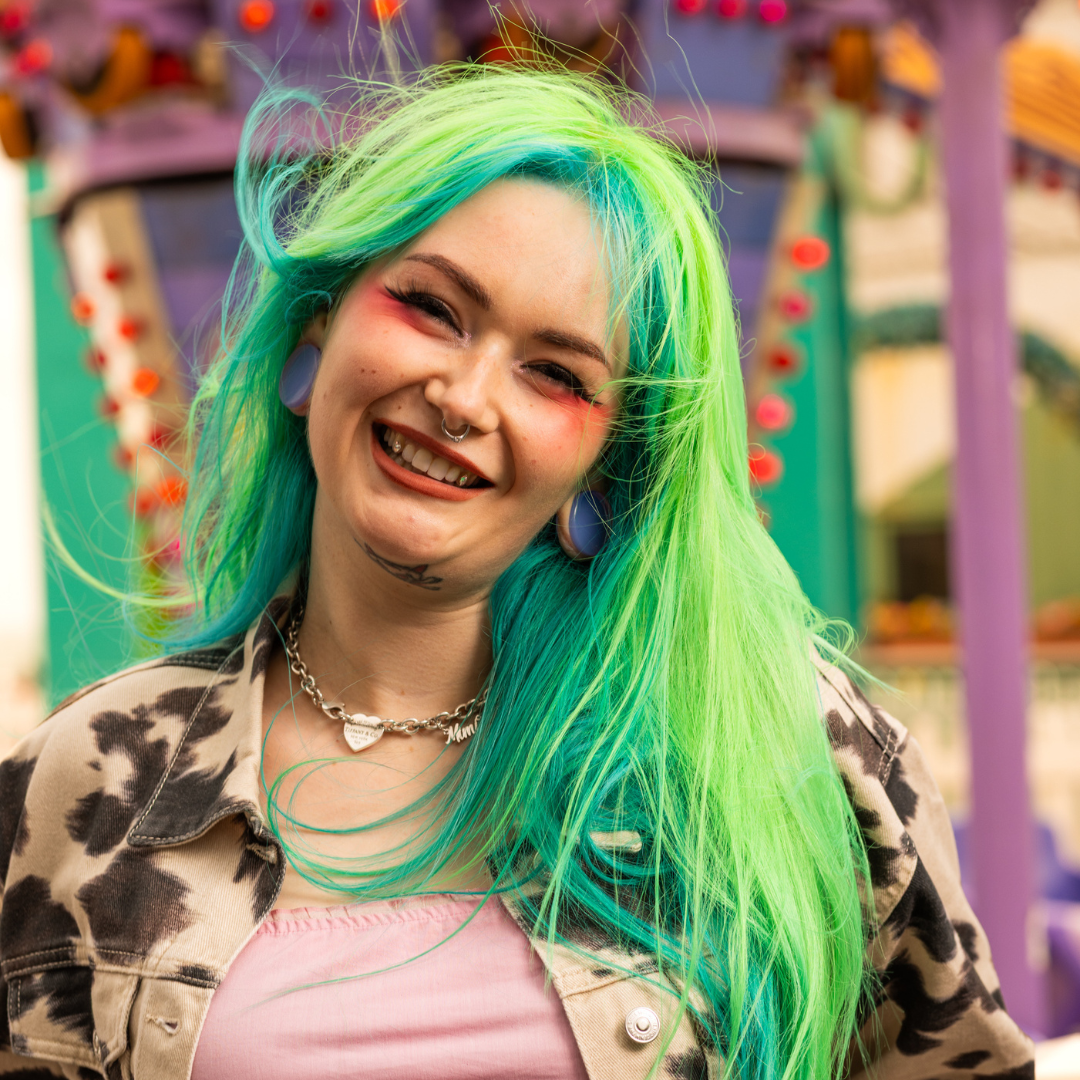 Crazy Color's Person with vibrant green and blue hair smiling in front of a colorful background by ABS France Wholesale 