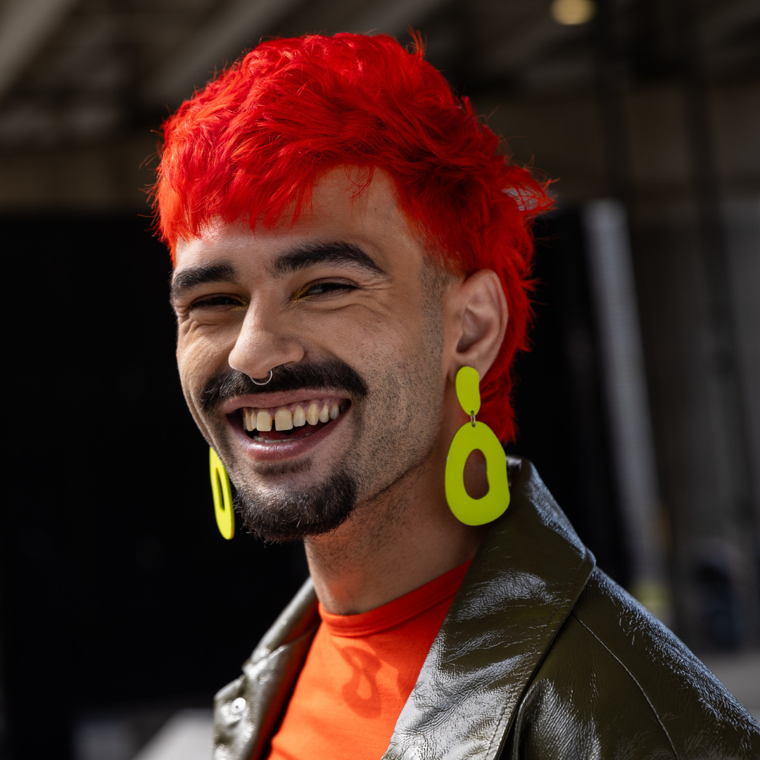 Crazy Color's Person with bright red hair and yellow earrings smiling outdoors by ABS France Wholesale