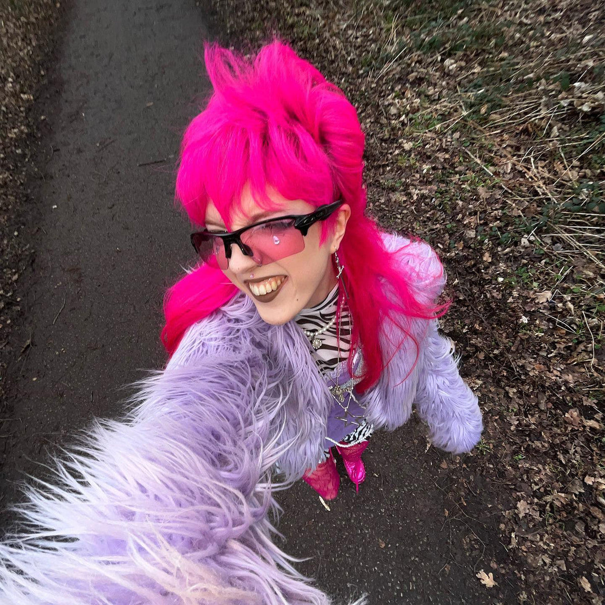 Crazy Color's Person with bright pink hair and a purple jacket standing outdoors on a path by ABS France Wholesale