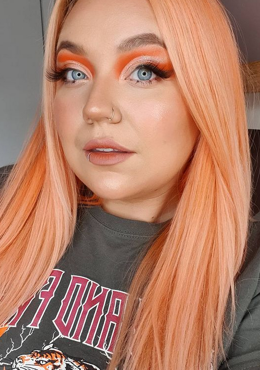 Crazy Color Person with peach hair and colorful makeup wearing a dark shirt with visible text by ABS France Wholesale