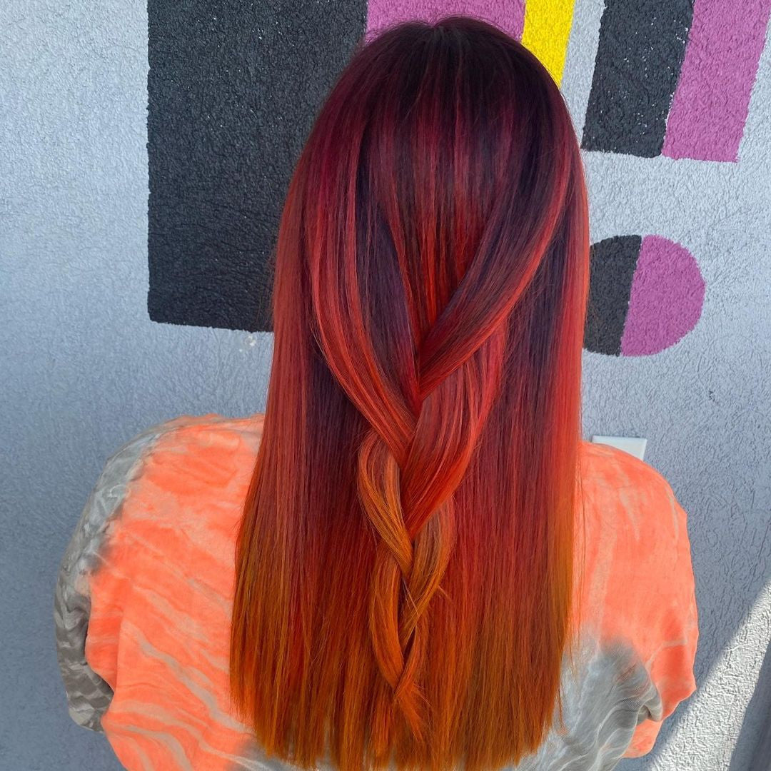 Crazy Color's Person with vibrant red and orange hair styled in a braid, wearing an orange top against a colorful abstract background by ABS France Wholesale