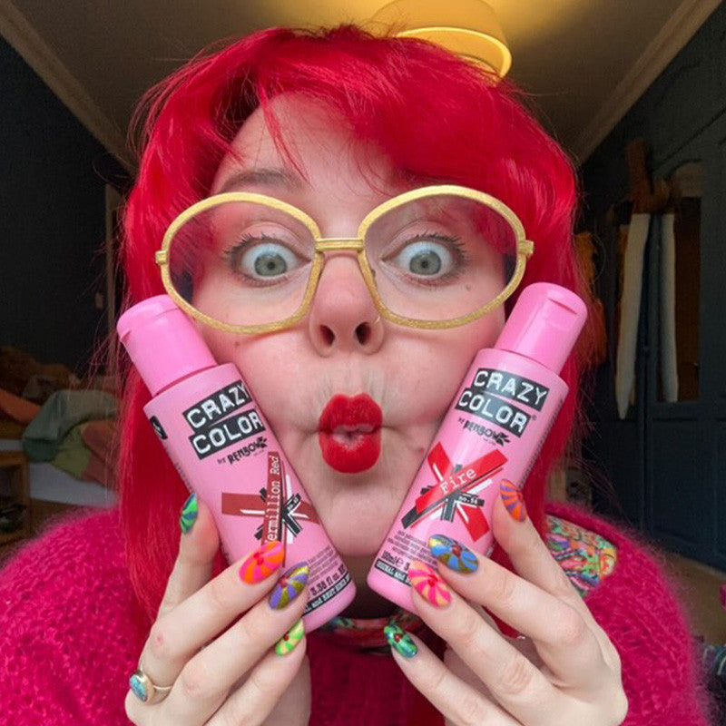Person with bright red hair and colorful nails holding bottles of Crazy Color's vermillion red and fire hair dye by ABS France Wholesale