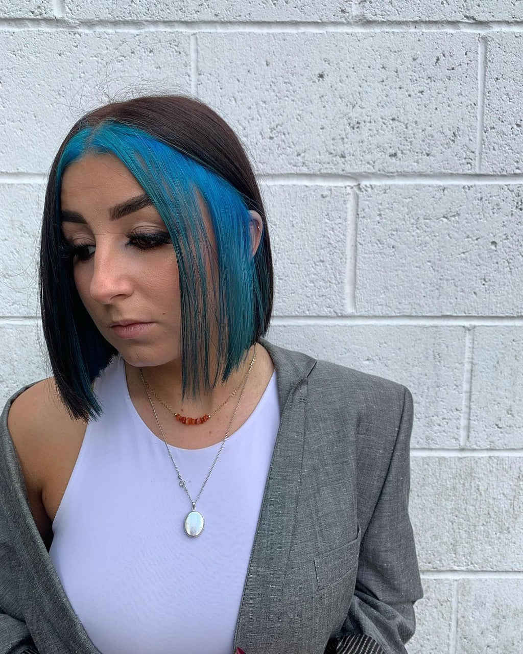 Crazy Color's person with blue hair and a gray blazer standing against a white brick wall by ABS France Wholesale