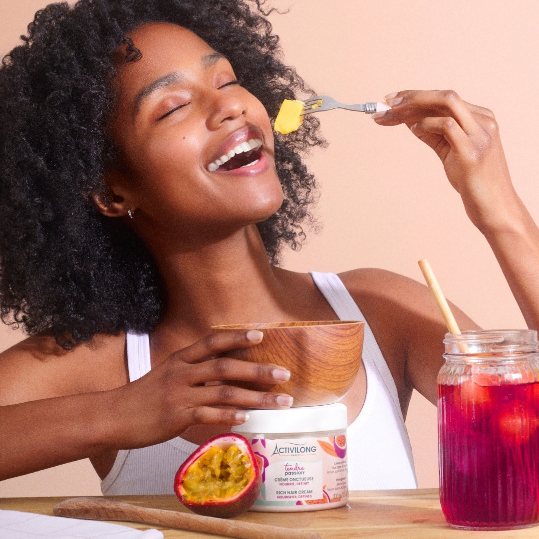 Woman eating from a bowl with a jar of ACTIVILONG TENDRE PASSION Crème Onctueuse 300ml by ABS France Wholesale and a fruit on a table.