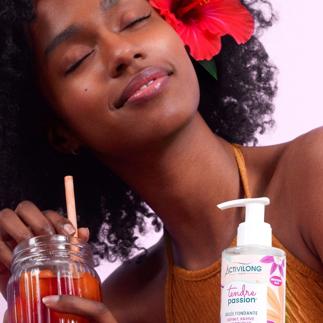 Woman with a flower in her hair holding a drink, next to a Bottle of ACTIVILONG TENDRE PASSION Gelée Fondante 260ml by ABS France Wholesale.