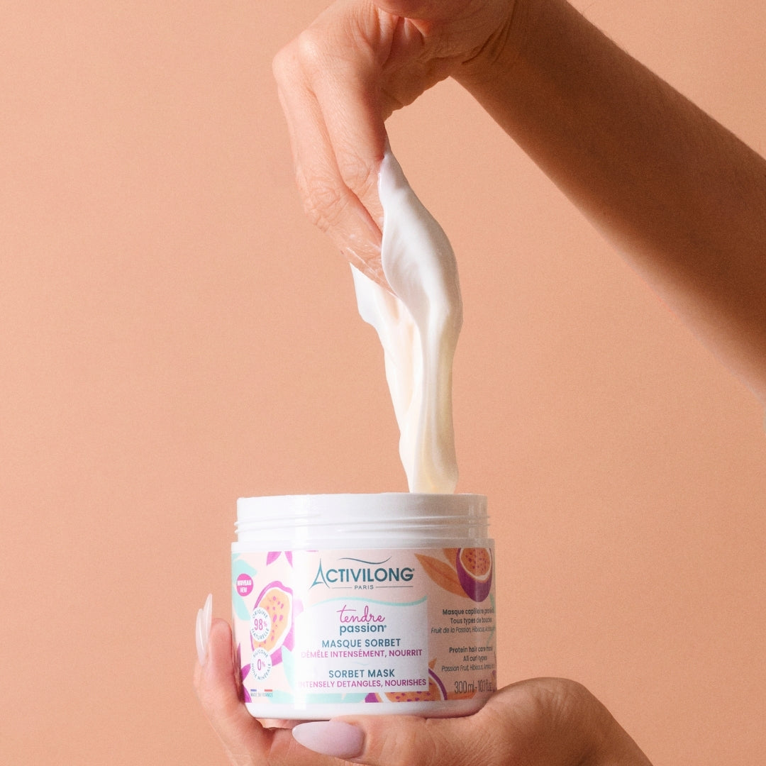 Hand holding an ACTIVILONG TENDRE PASSION Masque Sorbet 300ml jar by ABS France Wholesale with a spoonful being lifted, against a beige background