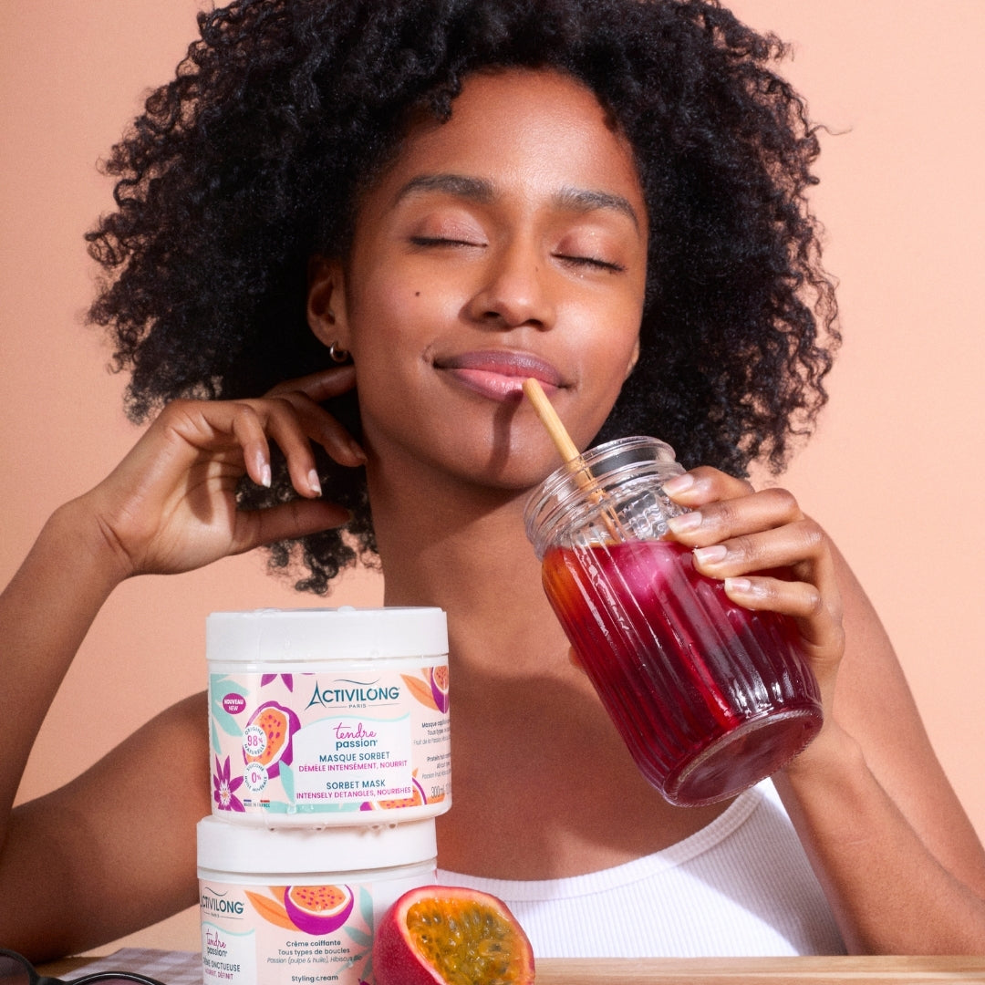 Woman enjoying a drink with ACTIVILONG TENDRE PASSION Masque Sorbet 300ml jars by ABS France Wholesale on a peach background