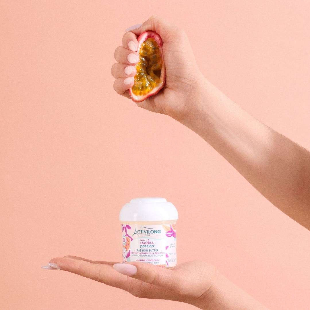 Hand holding an ACTIVILONG TENDRE PASSION Passion Butter 100ml Container by ABS France Wholesale with a passion fruit on a peach background