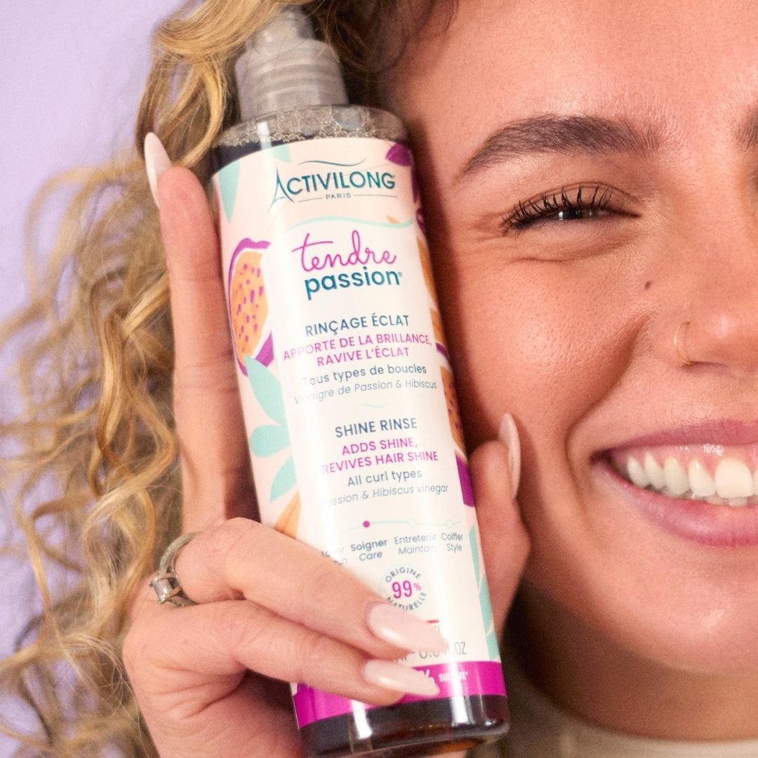 Woman holding an ACTIVILONG TENDRE PASSION Rinçage Éclat 250ml bottle by ABS France Wholesale with a purple background