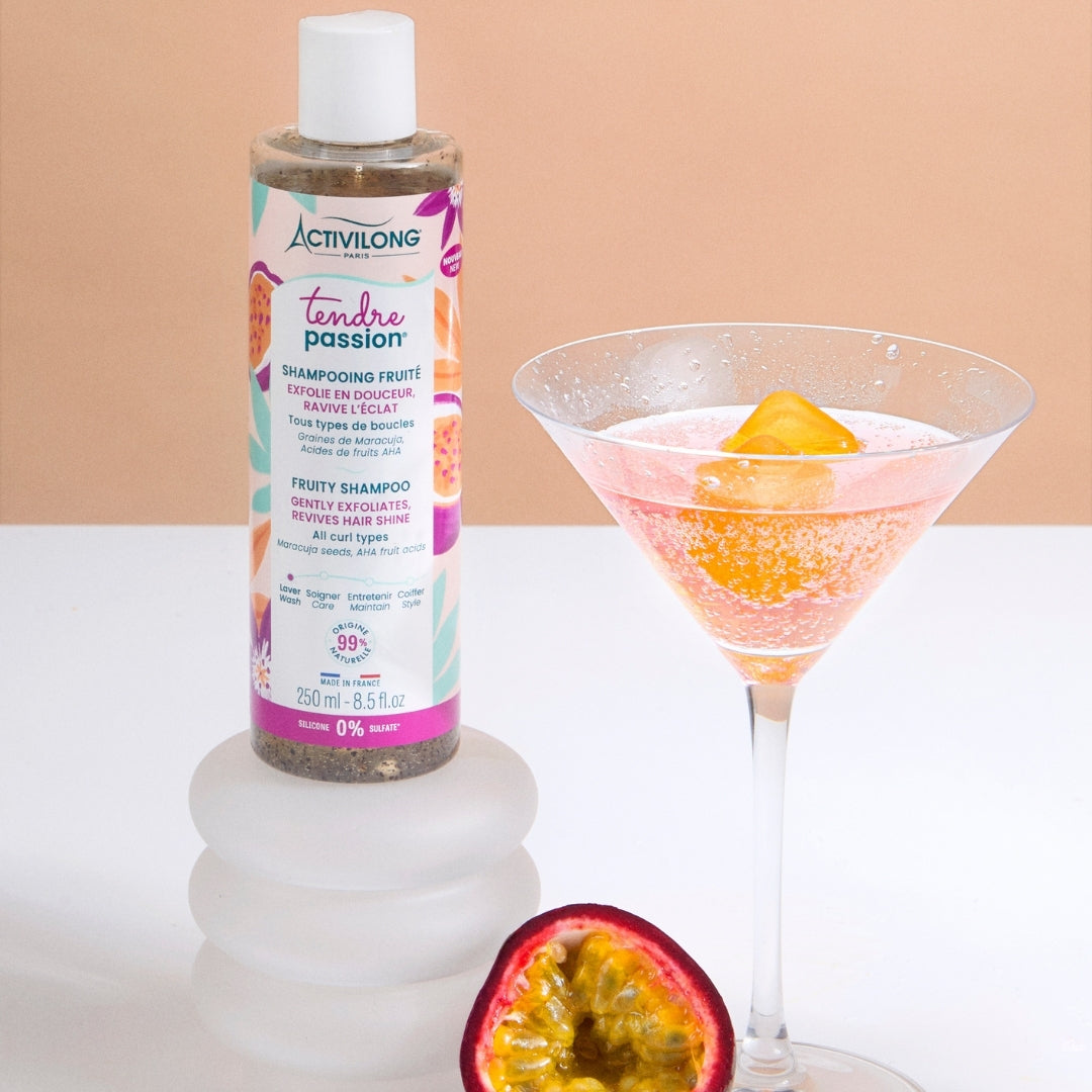 Bottle of ACTIVILONG TENDRE PASSION Shampooing Fruité 250ml by ABS France Wholesale next to a cocktail and passion fruit on a peach background