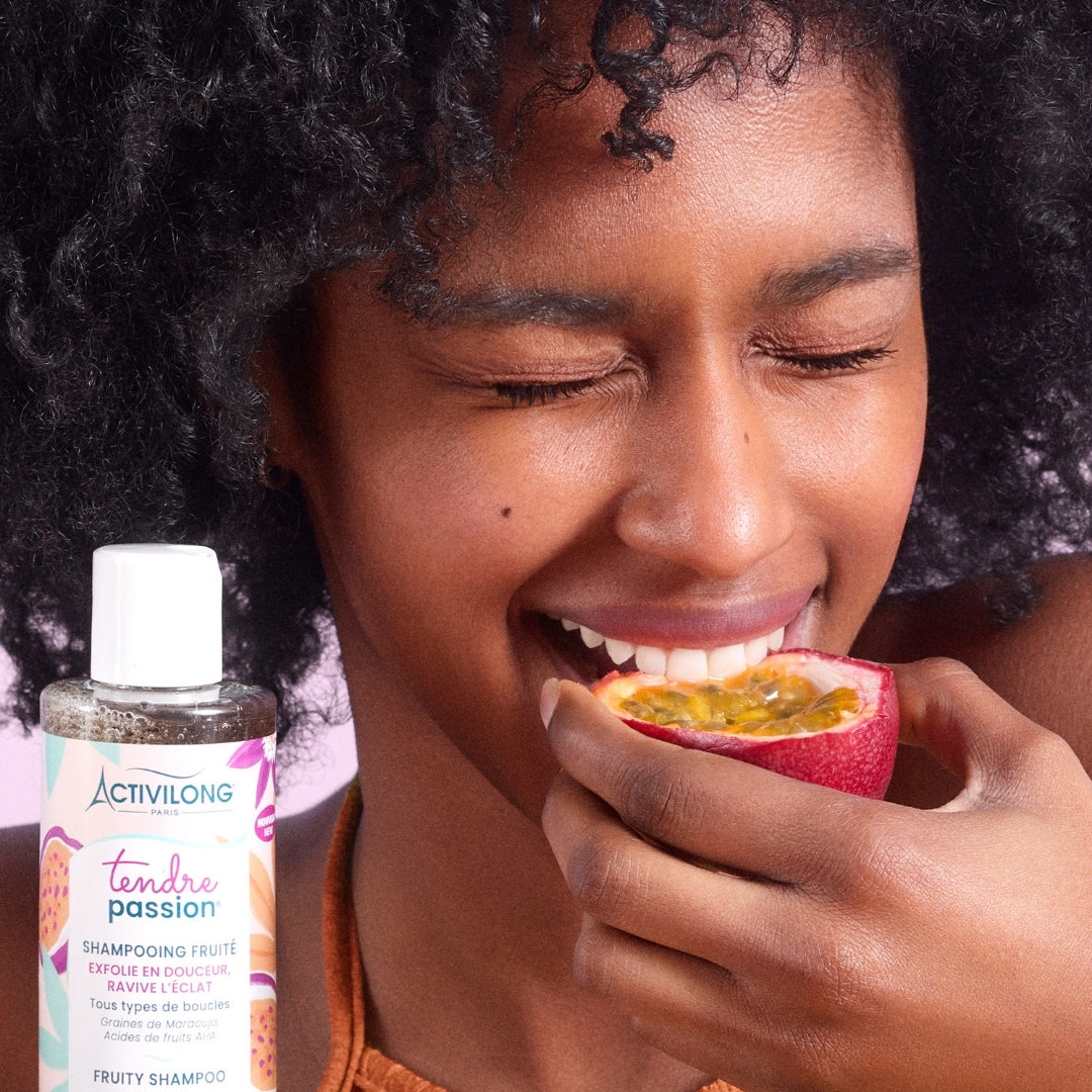 Woman eating a passion fruit with an ACTIVILONG TENDRE PASSION Shampooing Fruité 250ml by ABS France Wholesale next to her