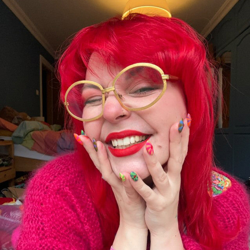 Person with red hair and pink sweater posing with hands on face in a casual setting - ABS France Wholesale