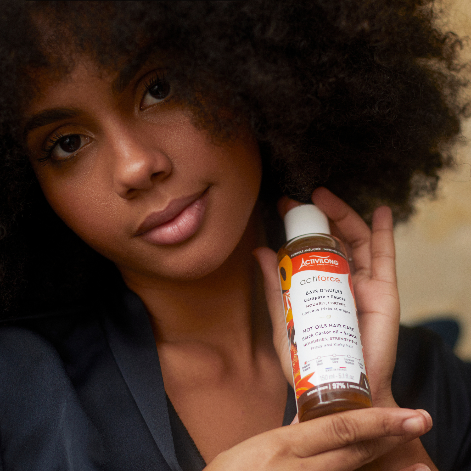 Woman holding an ACTIVILONG ACTIFORCE Bain d'Huile 130ml Bottle by ABS France Wholesale close to her hair