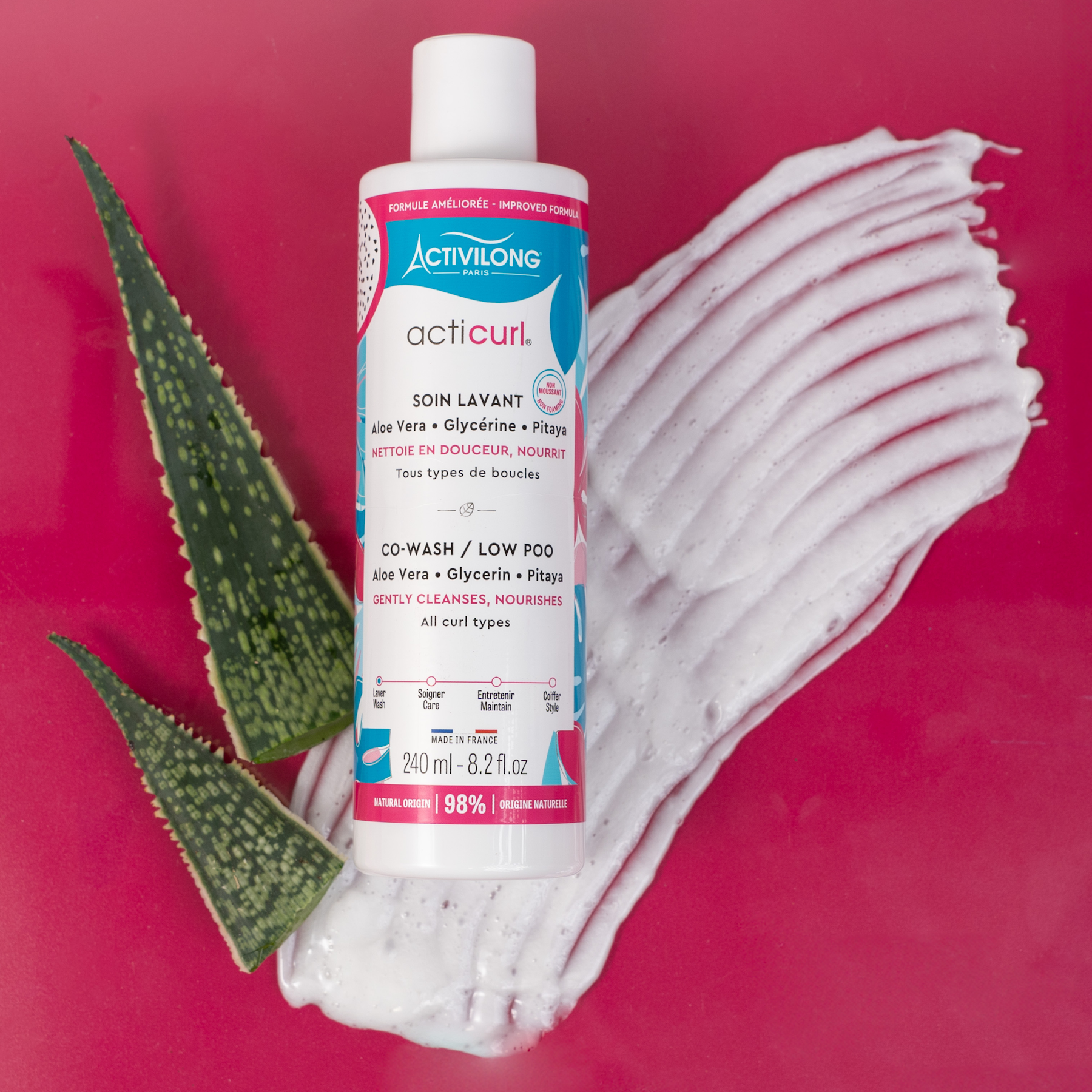 Bottle of ACTIVILONG ACTICURL Co-Wash 240ml by ABS France Wholesale with aloe vera leaf and foam on a red background