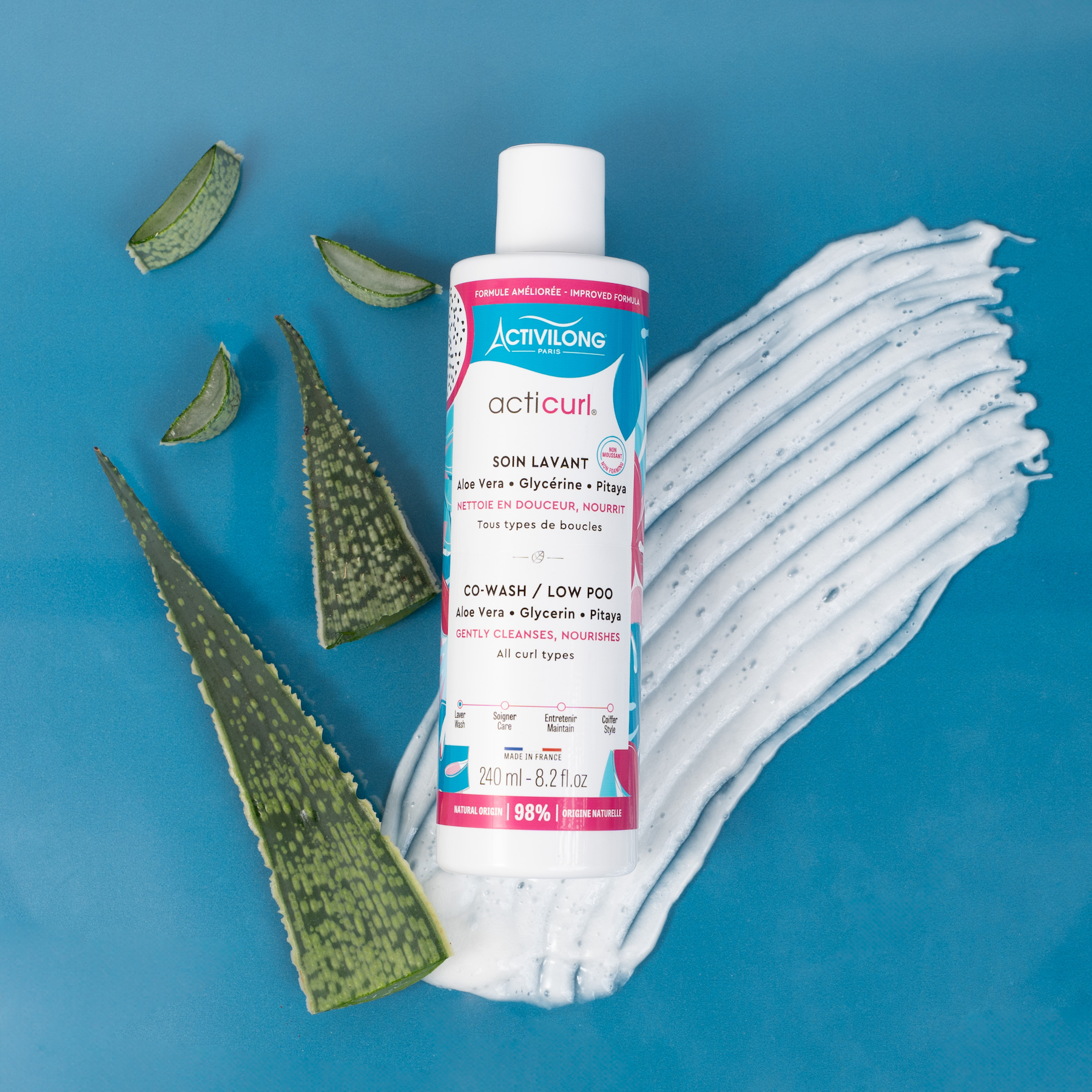 Bottle of ACTIVILONG ACTICURL Co-Wash 240ml by ABS France Wholesale with aloe vera leaves on a blue background