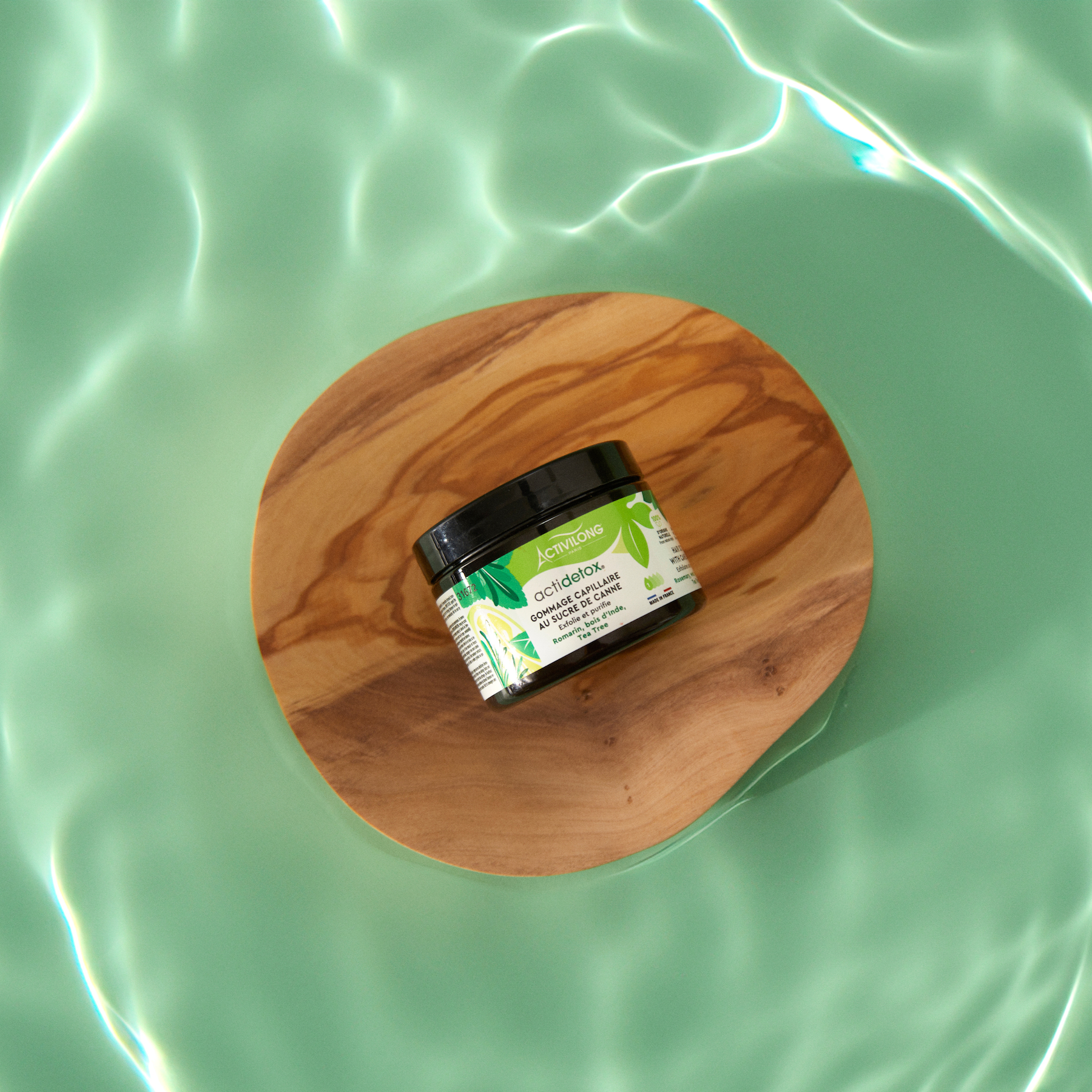 Jar of ACTIVILONG ACTIDETOX Gommage Capillaire 150ml by ABS France Wholesale on a wooden disc over green water
