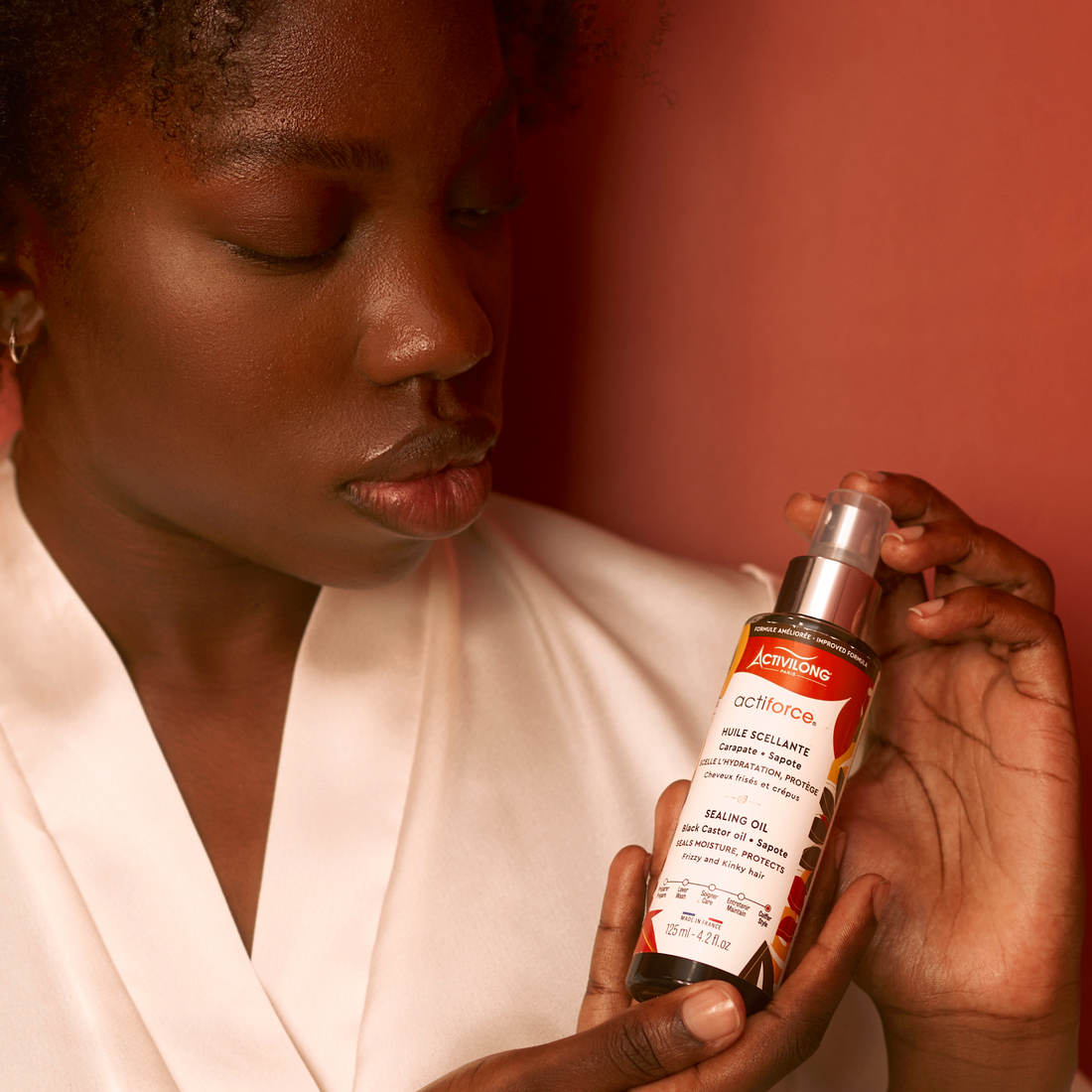 Woman holding an ACTIVILONG ACTIFORCE Huile Scellante 125ml bottle by ABS France Wholesale with a red background
