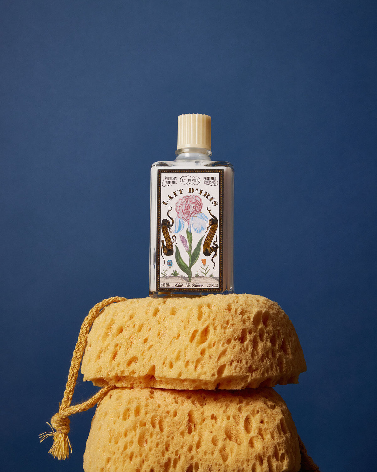 Bottle of Lait d'iris perfume on a yellow sponge against a blue background
