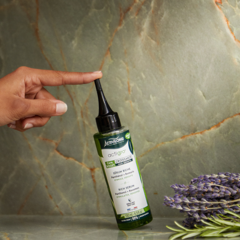 Hand holding a bottle of ACTIVILONG ACTIGRO Sérum Riche 130 ml bottle by ABS France Wholesale with lavender flowers on a marble background