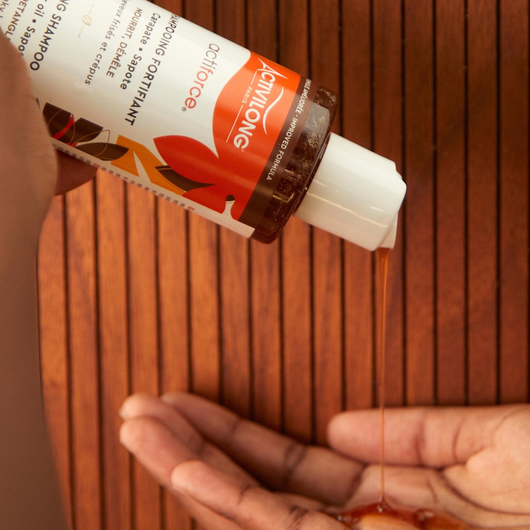 Person pouring a liquid from an ACTIVILONG ACTIFORCE Fortifiant Shampoing 250ml bottle by ABS France Wholesale into their hand against a wooden background.
