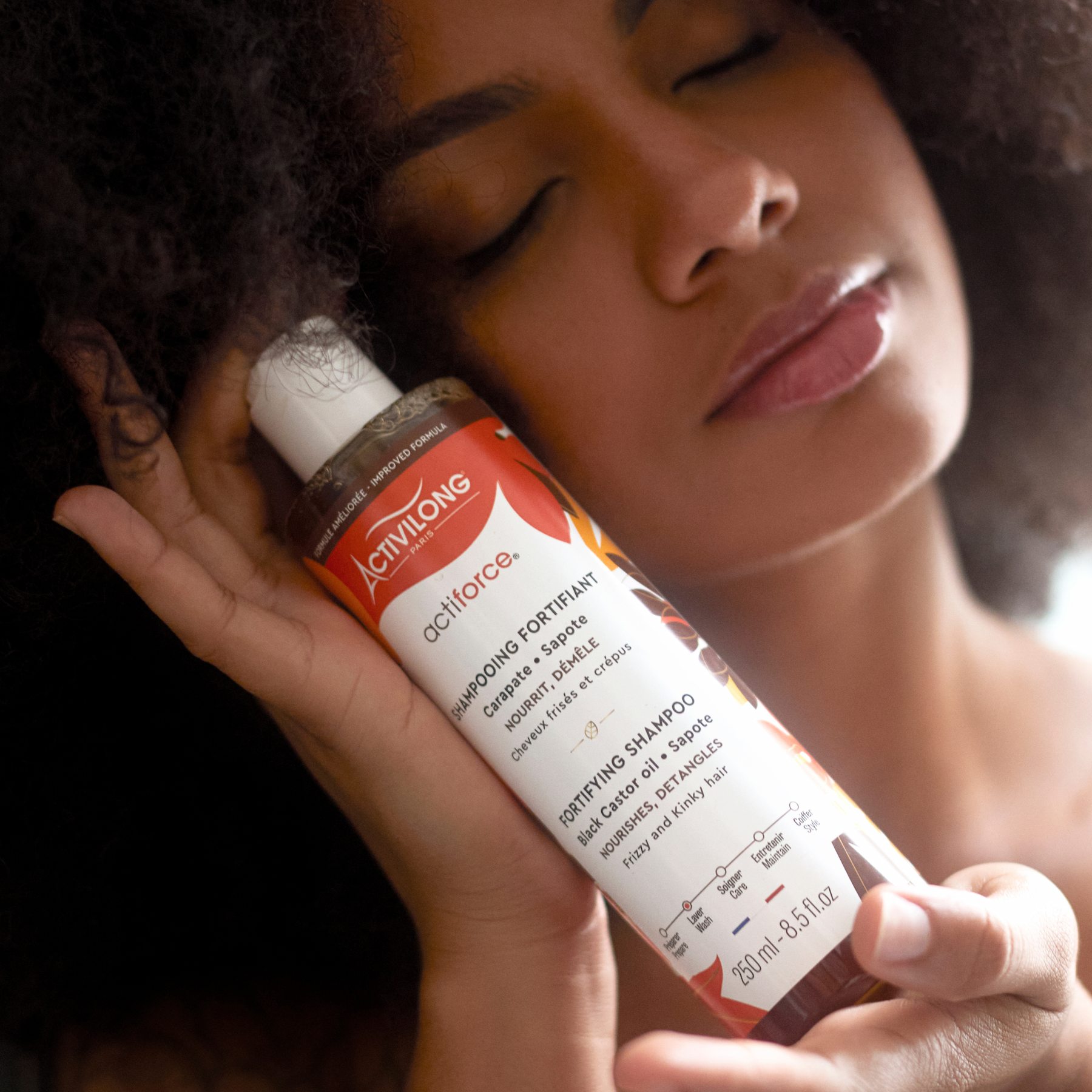 Person holding an ACTIVILONG ACTIFORCE Fortifiant Shampoing 250ml bottle by ABS France Wholesale close to their hair