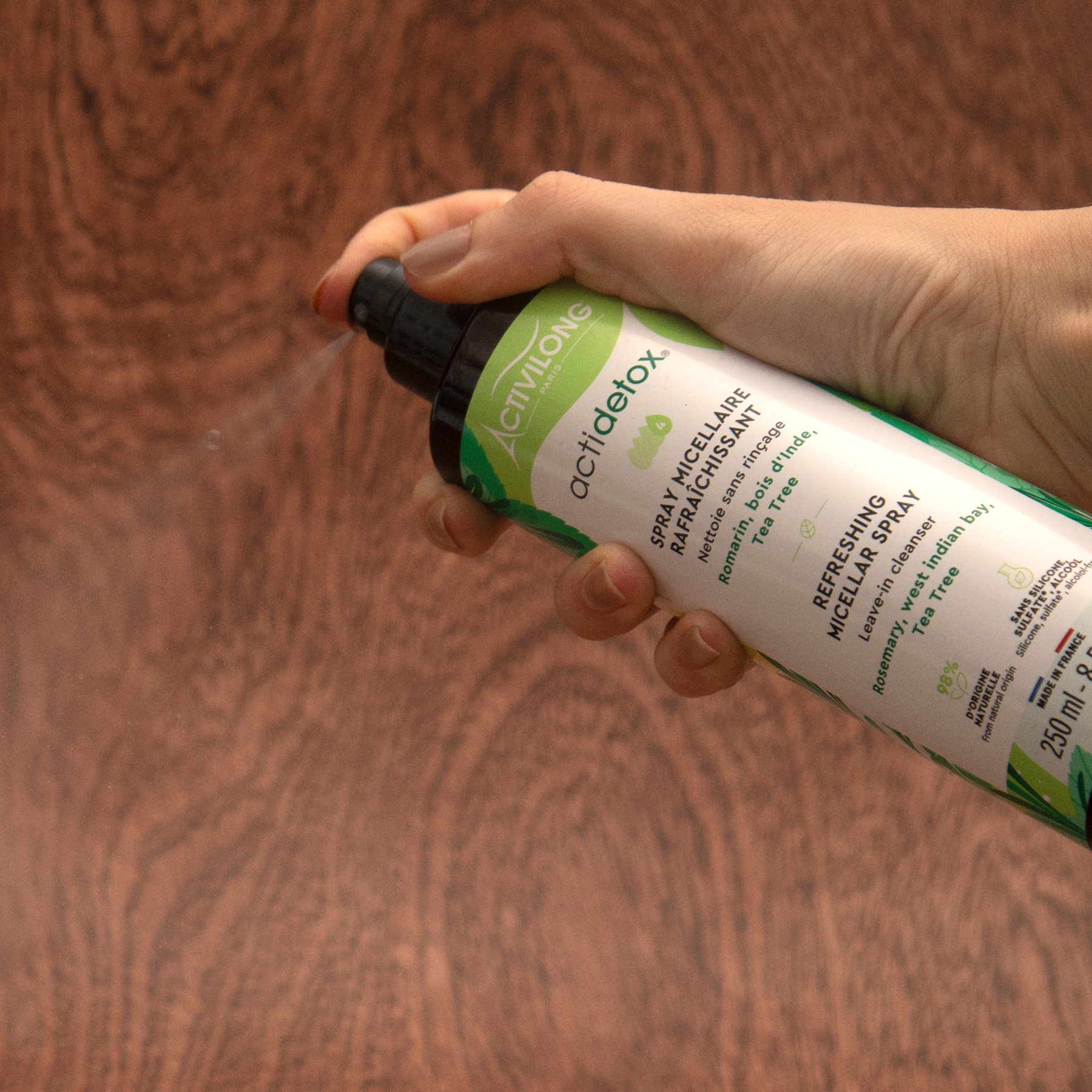 Hand holding a bottle of ACTIVILONG ACTIDETOX Spray Micellaire Rafraîchissant 250ml by ABS France Wholesale against a wooden background