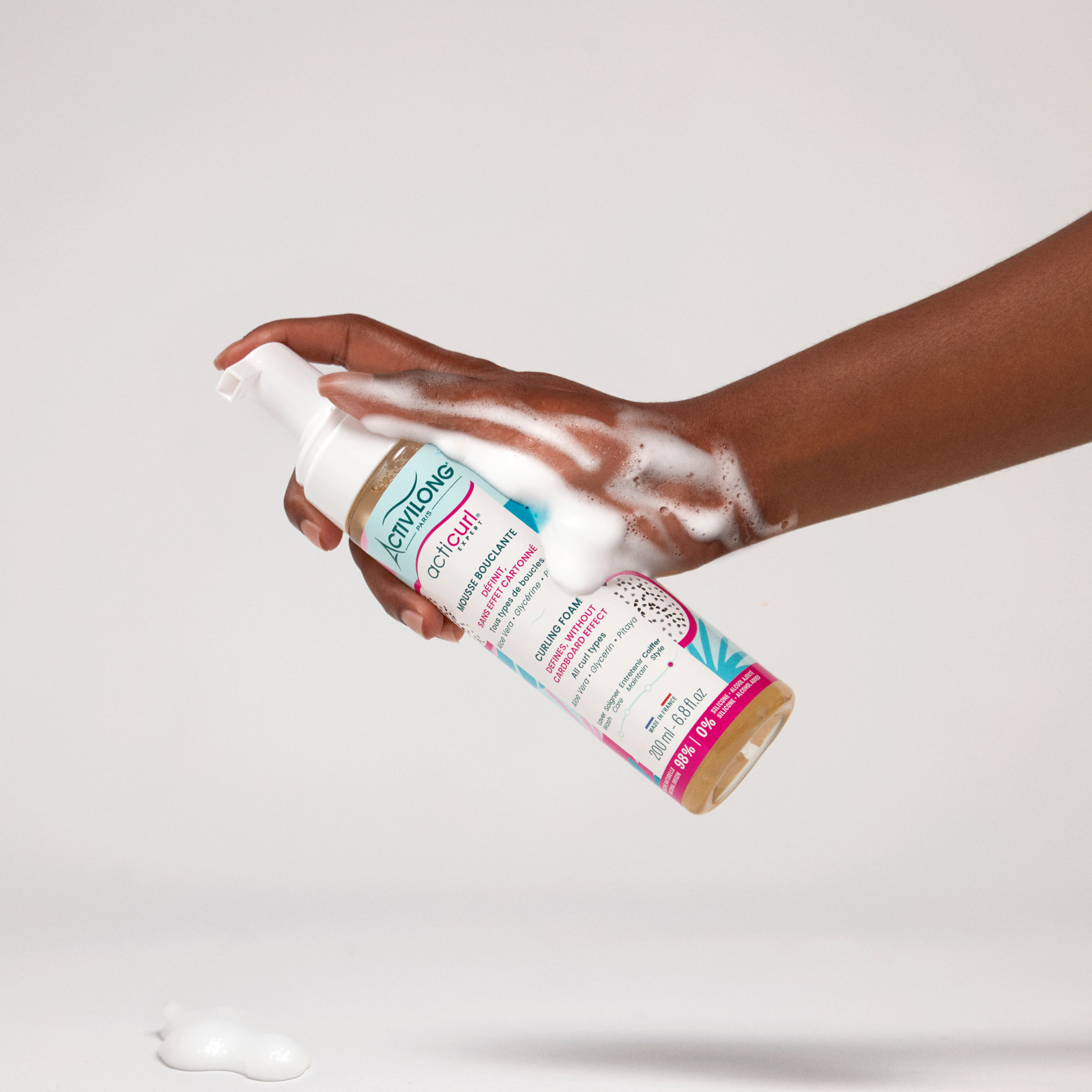 Hand holding a ACTIVILONG ACTICURL EXPERT Mousse Bouclante 200ml bottle by ABS France Wholesale with a white background
